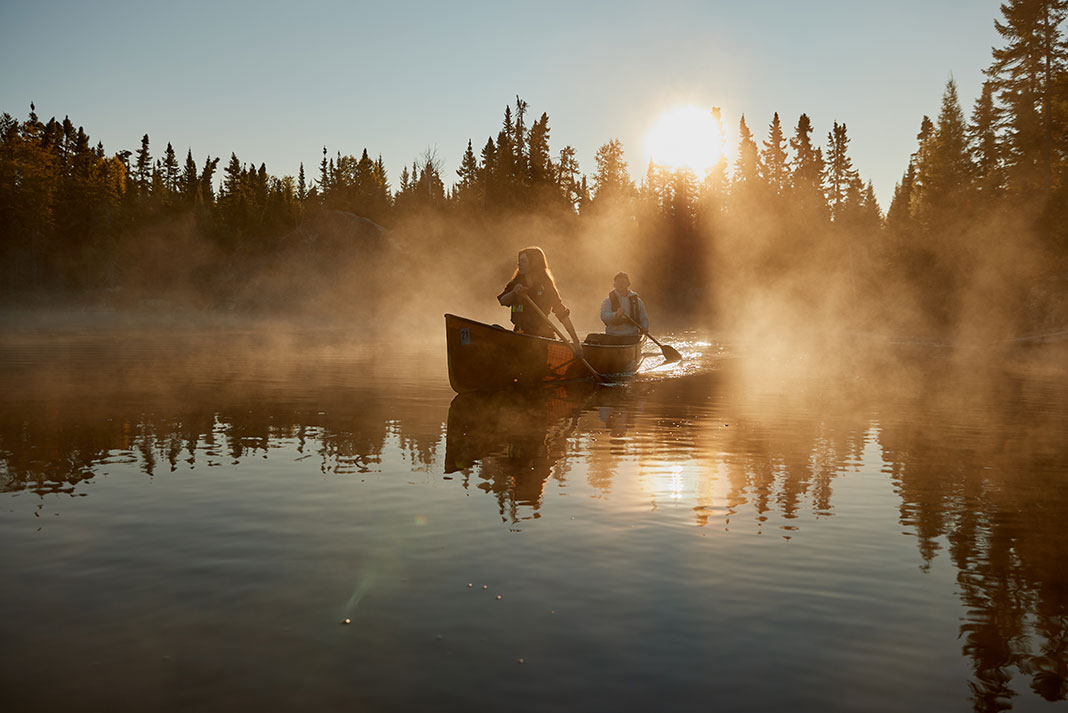 canoeists paddle through early morning mist in Minnesota's Boundary Waters Canoe Area