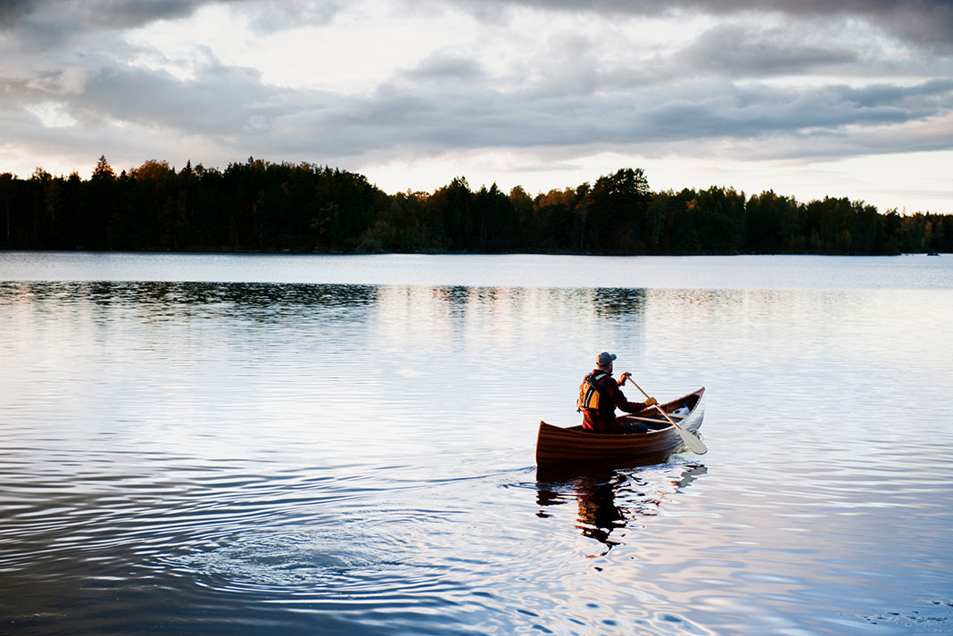 a canoeist paddles on calm lake under clouds