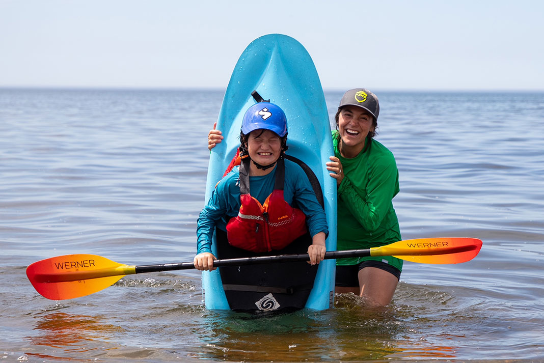 a woman holds up a Jackson whitewater kayak with a kid inside holding a Werner paddle