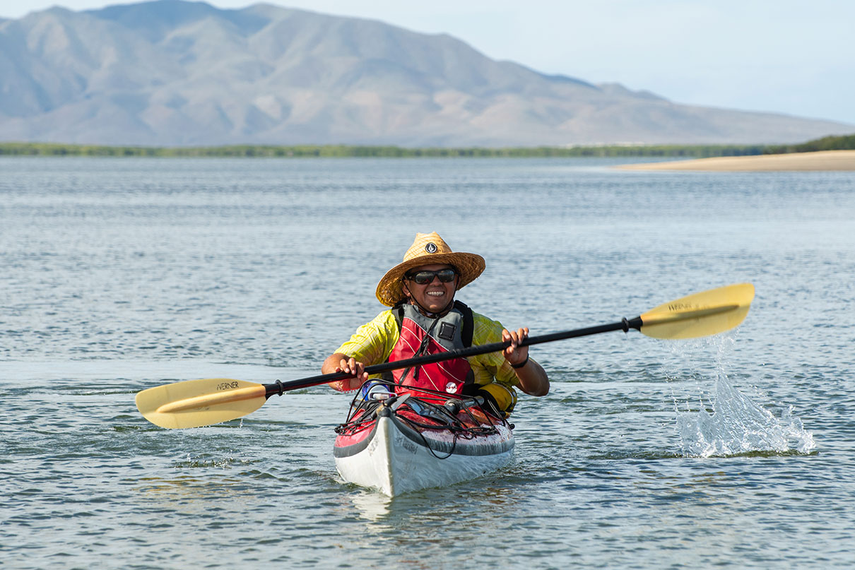 a man smiles as he paddles his sea kayak in the sun