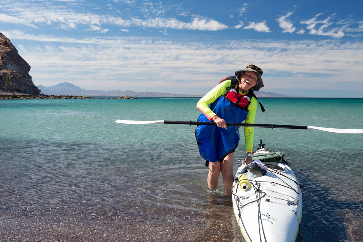 woman poses with kayak and smiles on Baja beach