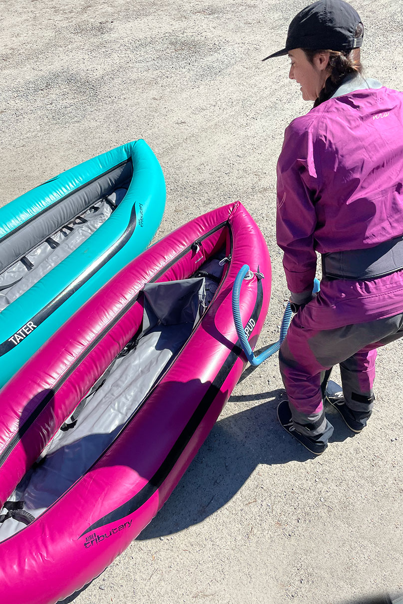 woman in purple drysuit pumps up the AIRE Spud with Tater inflated beside it