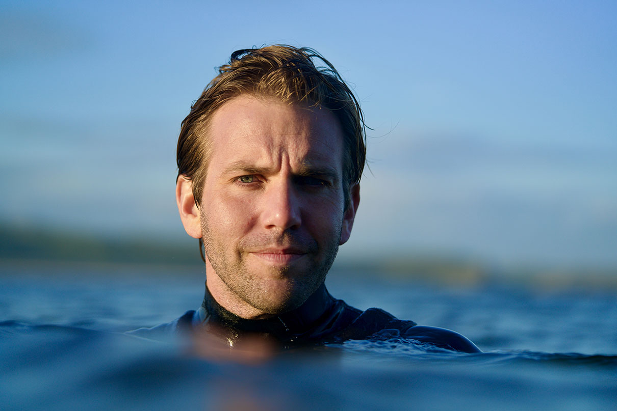 Headshot of biologist, author and filmmaker Tom Mustill as he is shoulder-deep in water