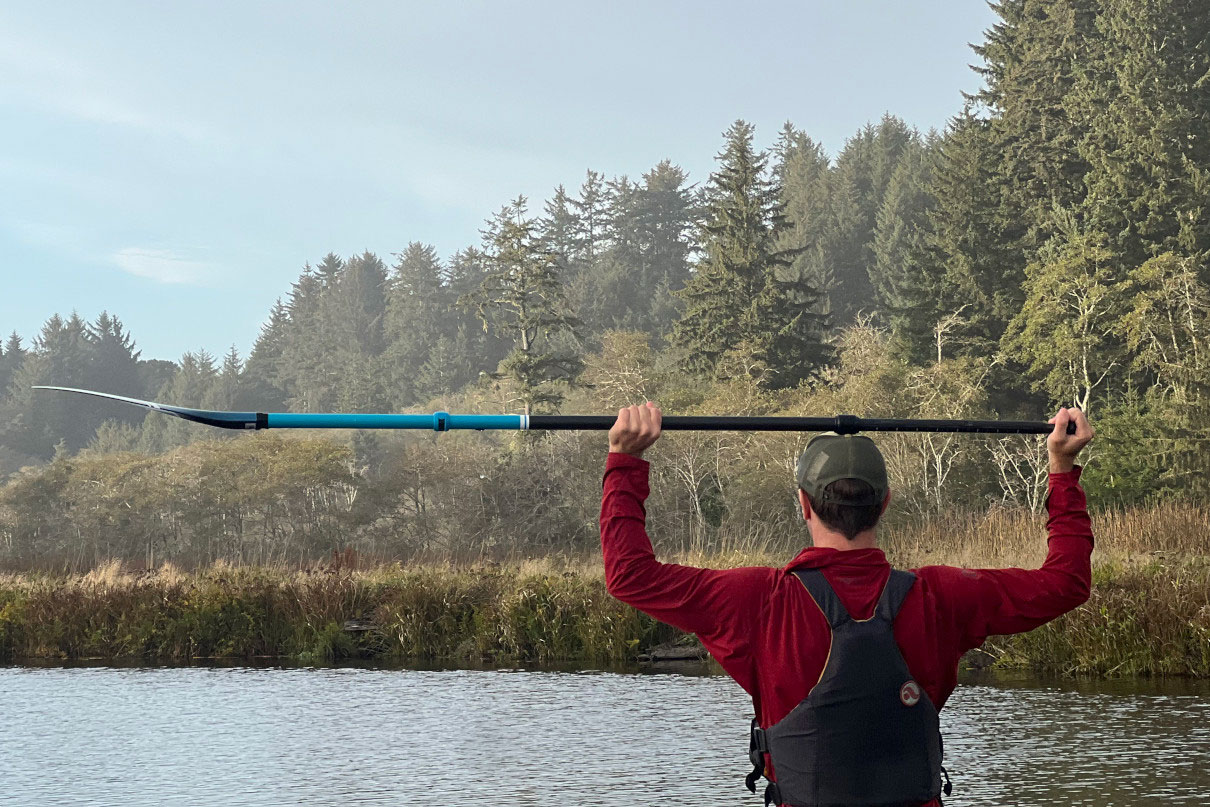 man stands holding paddleboard paddle on his head with both elbows bent at 90 degrees