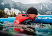 man immersed in water beside his paddleboard while wearing a Mustang Khimera inflatable PFD