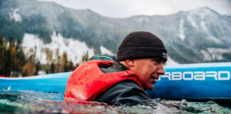 man immersed in water beside his paddleboard while wearing a Mustang Khimera inflatable PFD