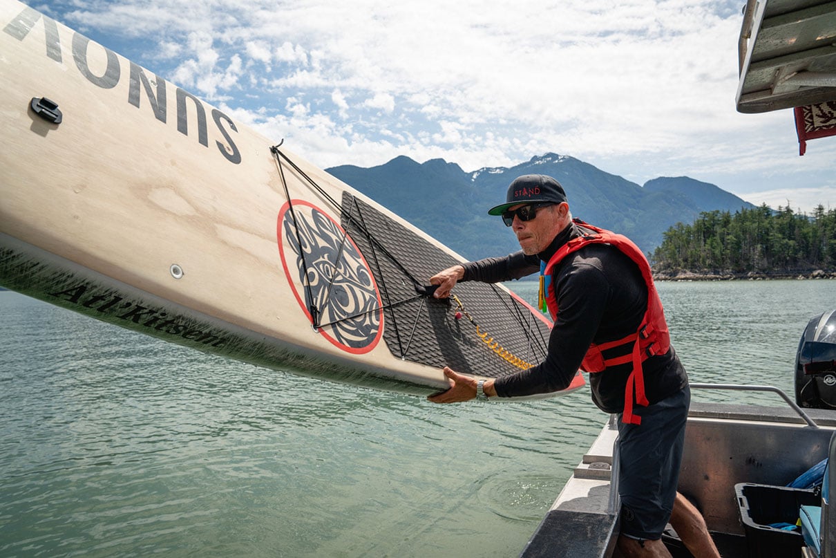 man prepares to launch inflatable paddleboard while wearing a Khimera inflatable PFD