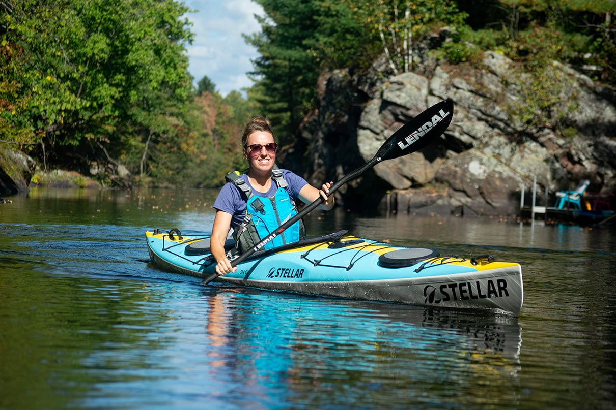 woman paddles the Stellar S14 G2 touring kayak near rocks and trees