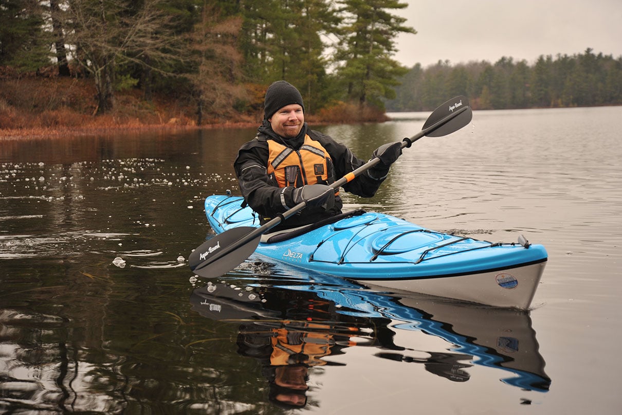 man paddles the Delta 14 touring kayak in chilly fall weather while wearing hat and gloves