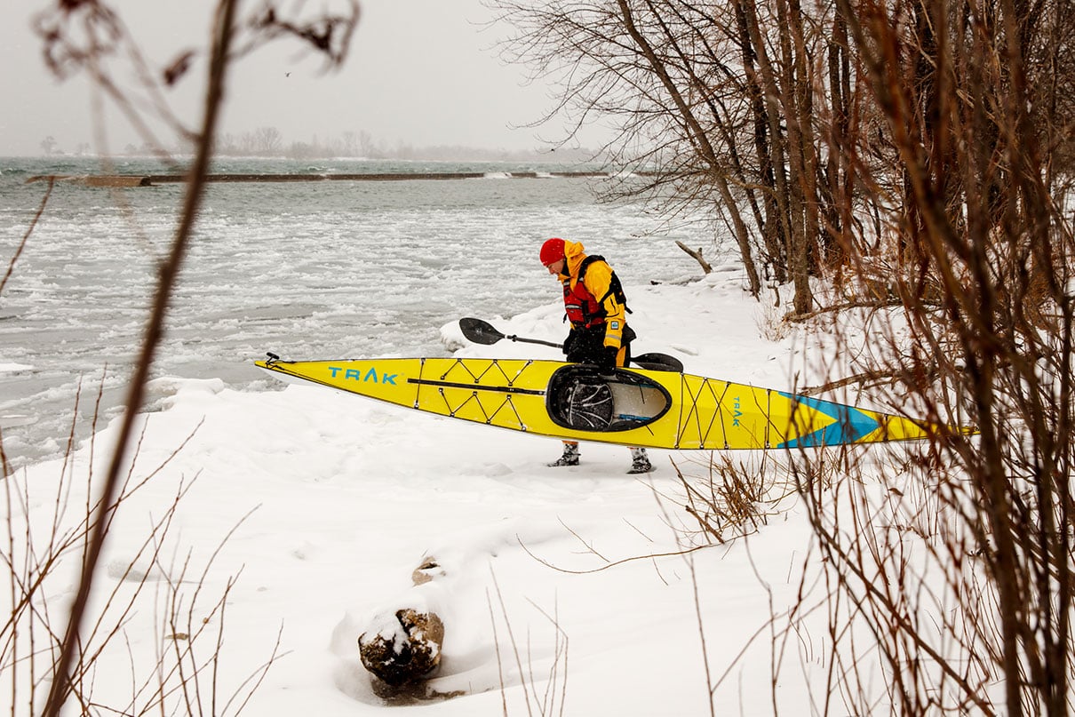 man carries the TRAK 2.0 touring kayak to the water's edge through snow in winter