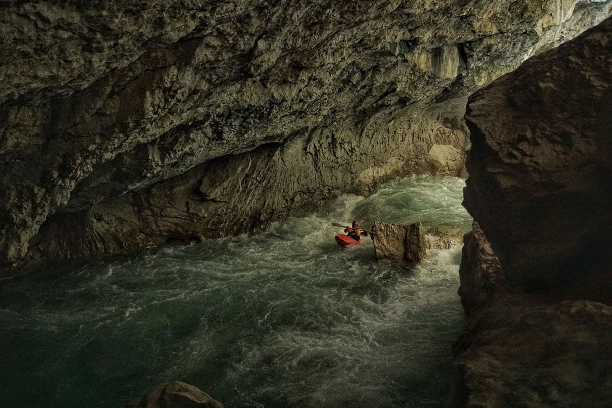 a person whitewater kayaks through a dramatically lit cavern