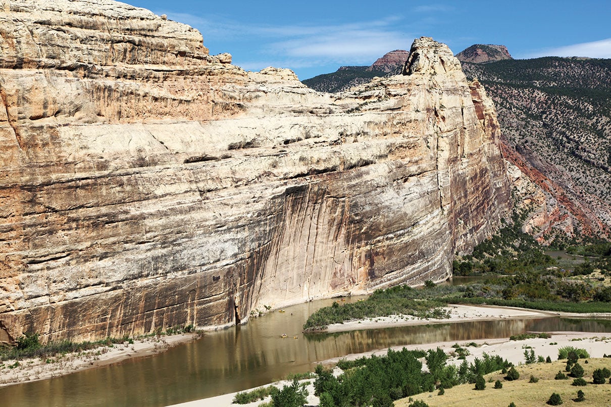 a dramatic rock wall beside river with tiny paddlers