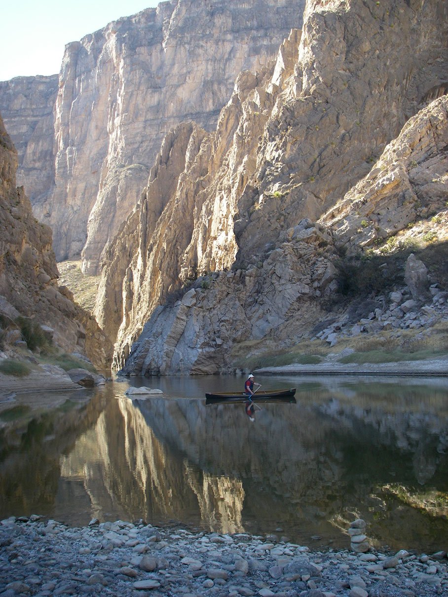 canoeist paddles on glassy water in a rocky canyon